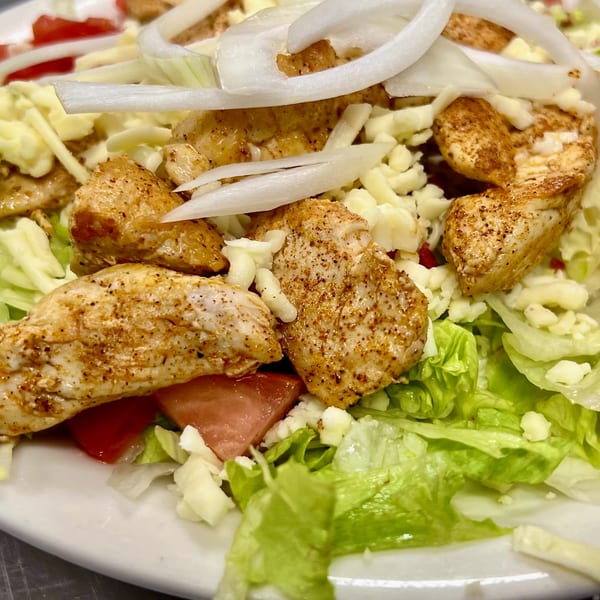 Close-up of a chicken salad with lettuce, tomatoes, onions, and shredded cheese.