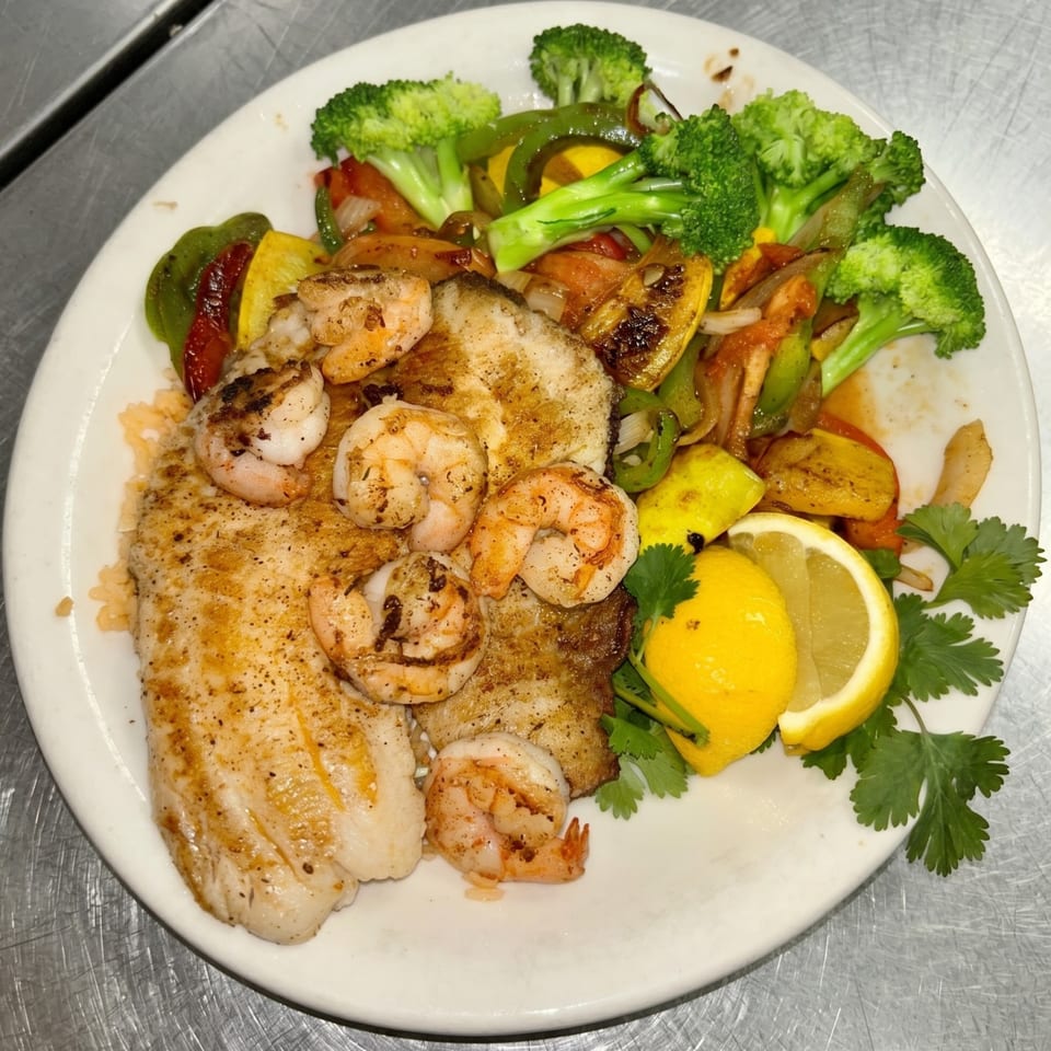 Grilled fish and shrimp with broccoli, bell peppers, and lemon wedges on a white plate.
