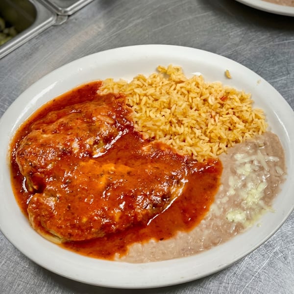 A white plate with chicken enchiladas covered in red sauce, rice, and refried beans.