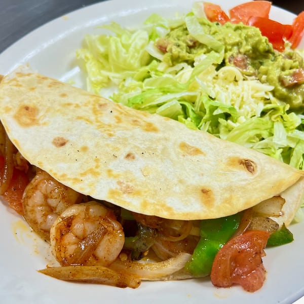 Shrimp fajita taco with sautéed onions and peppers, served with a side of lettuce, guacamole, and tomatoes.
