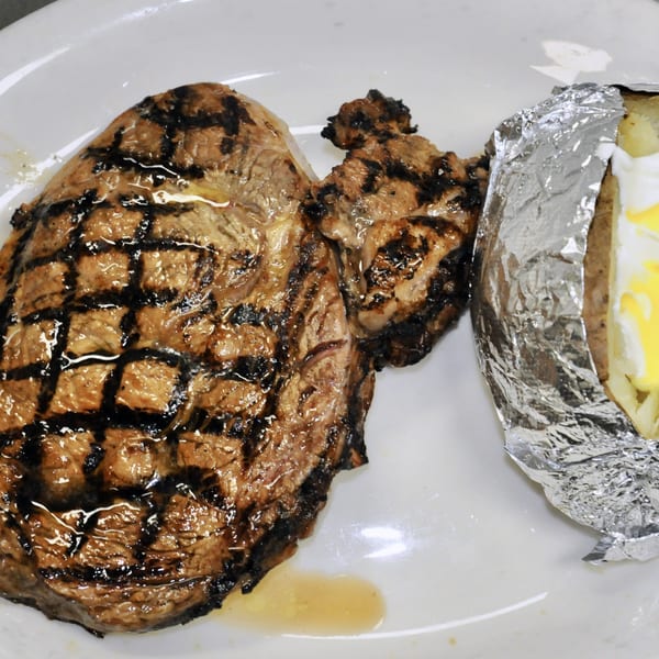 Grilled steak with prominent grill marks and a foil-wrapped baked potato with butter and sour cream.