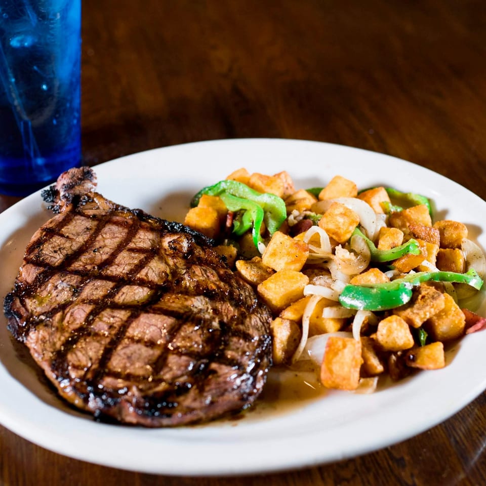 Grilled steak with grill marks, served with diced potatoes, green peppers, and onions on a white plate.