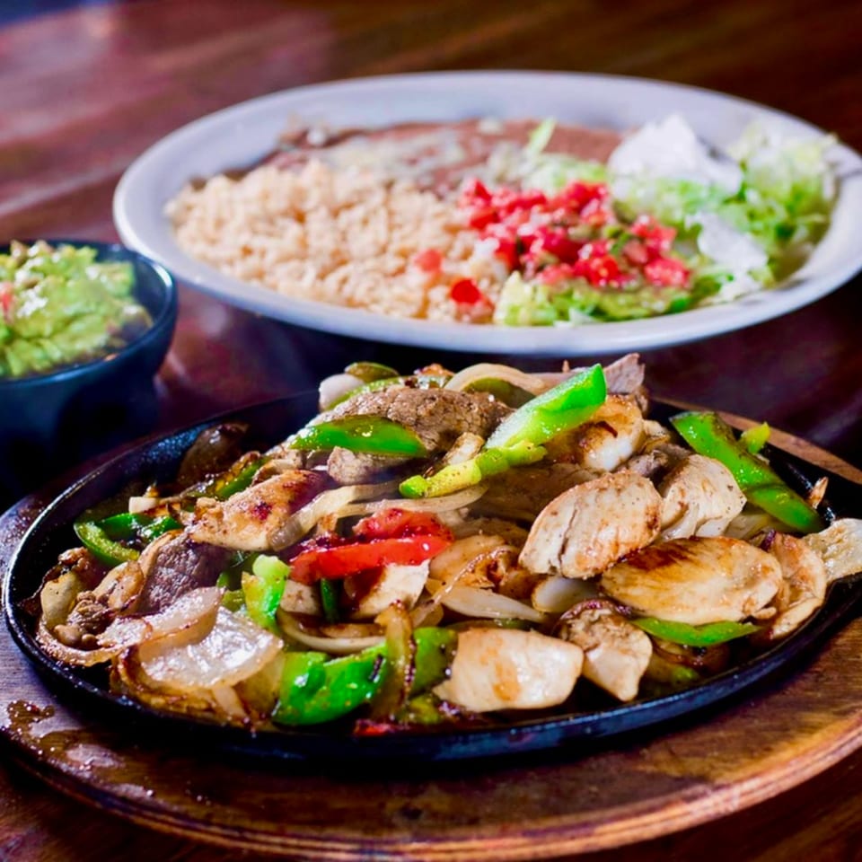 Sizzling fajitas with chicken, steak, peppers, and onions, served with rice, beans, and guacamole.