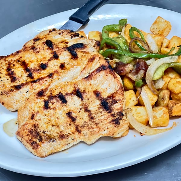 Grilled chicken breasts with charred marks, served with roasted potatoes, green peppers, and onions.